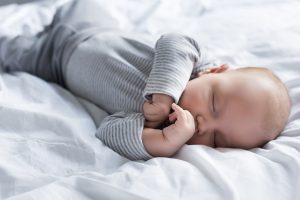 a baby sleeping tightly in white bed